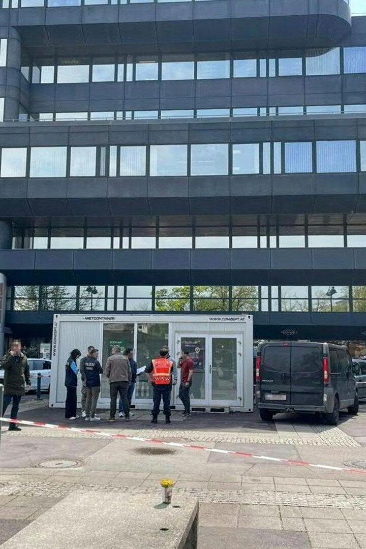 Mehrere Polizisten und Personen stehen vor einem abgesperrten Bereich vor einem modernen Bürogebäude.