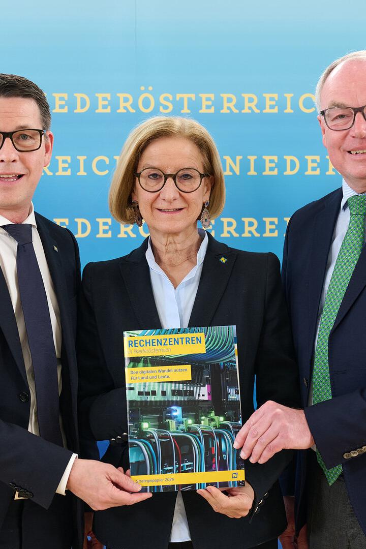 Drei Personen präsentieren eine Broschüre über Rechenzentren in Niederösterreich vor blauem Hintergrund.