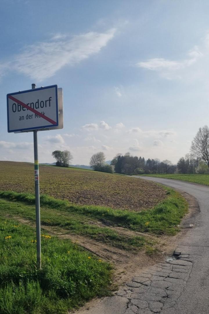 Ortsschild von Oberndorf an der Melk am Rand eines Feldes mit angrenzender Landstraße.