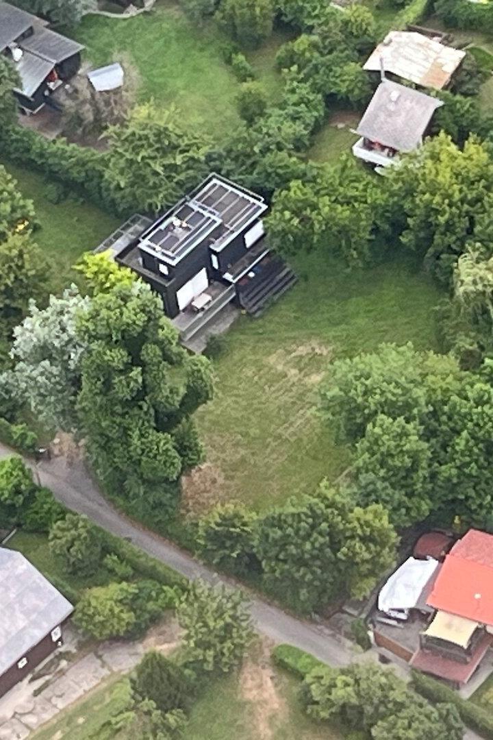 Luftaufnahme von Wohnhäusern mit Gärten und Bäumen in einer grünen Landschaft.