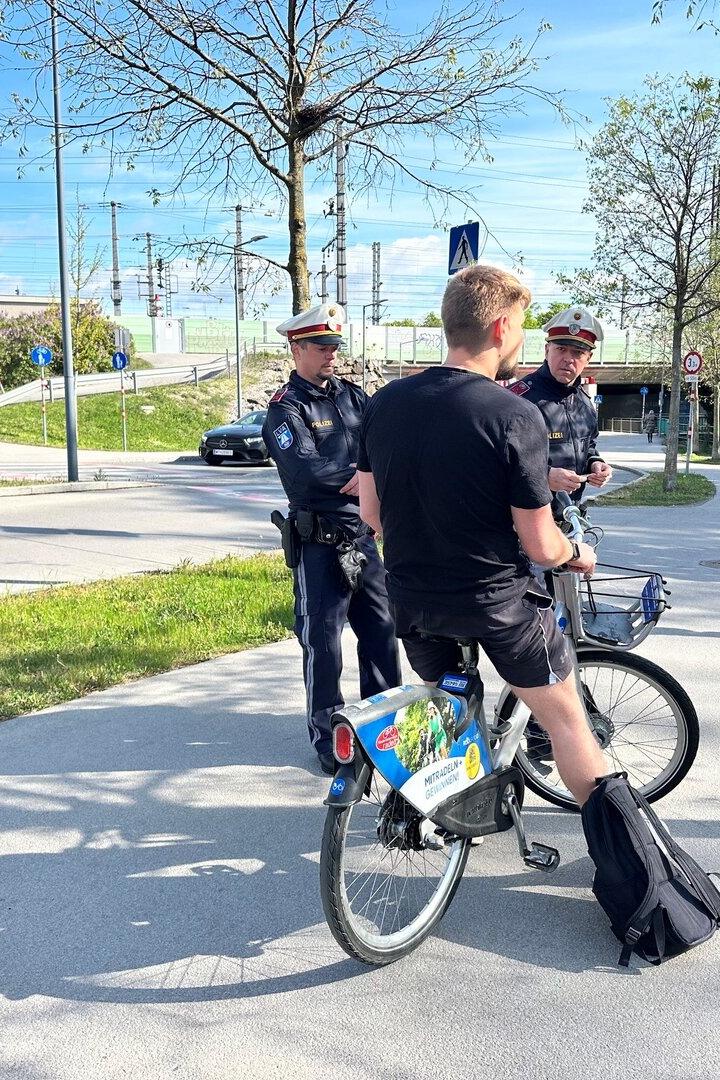 Ein Radfahrer wird von zwei Polizisten auf einem Weg angehalten.