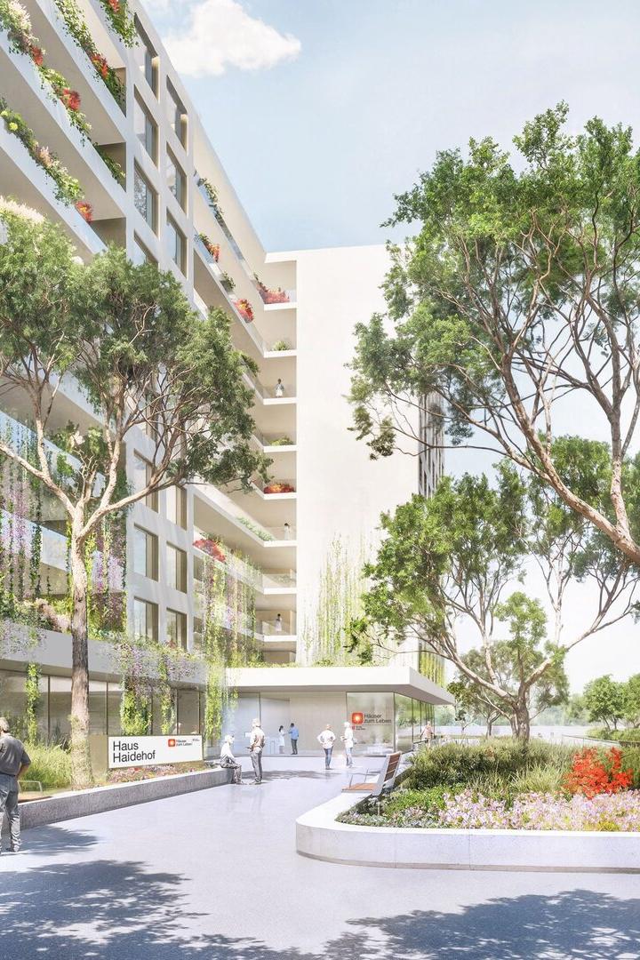 Mehrstöckiges modernes Gebäude mit großen Fenstern, umgeben von Bäumen, Blumenbeeten und Sitzbänken, Menschen im Außenbereich.