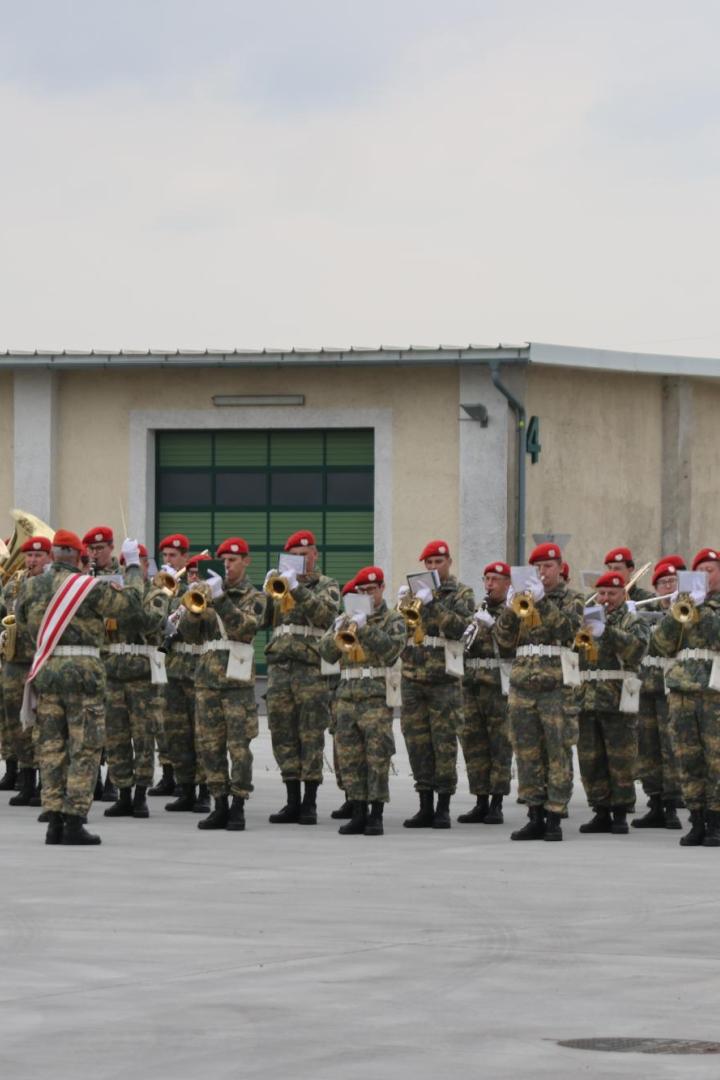 Militärmusiker in Tarnuniform und roten Baretten spielen auf dem Hof einer Kaserne.