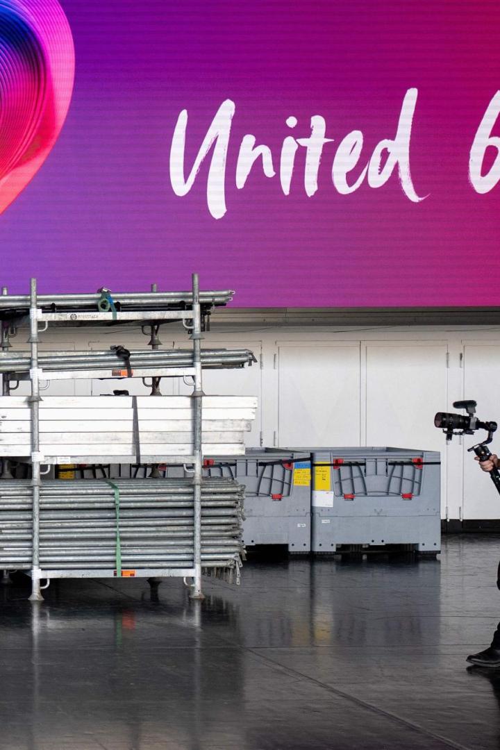 Eurovision Song Contest 2026 Ein Mann mit Kamera läuft vor einer großen bunten Herzgrafik und dem Schriftzug „United by Music“.