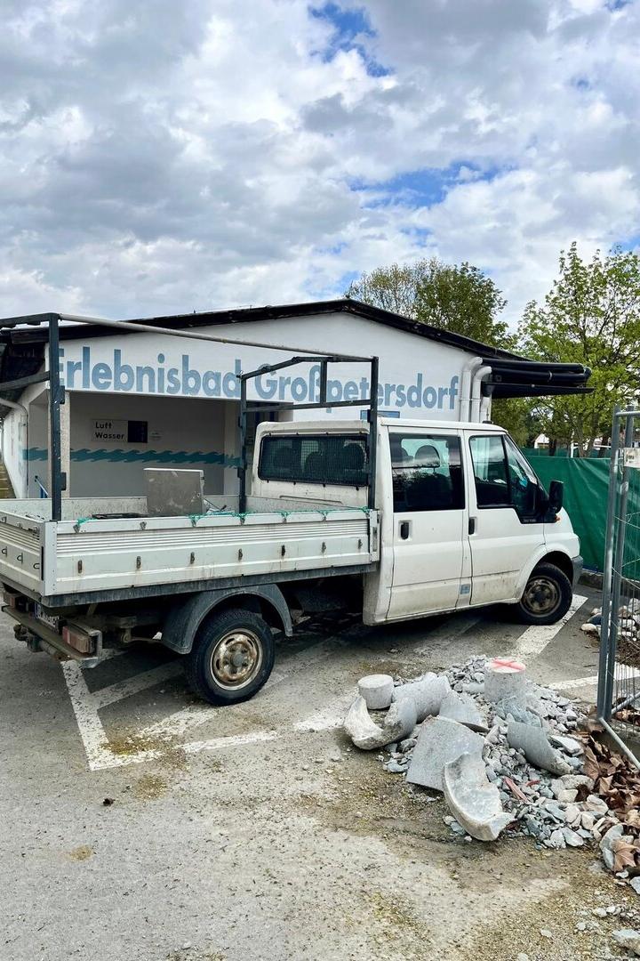 Ein weißer Transporter steht vor einem Gebäude mit der Aufschrift „Erlebnisbad Großpetersdorf“, daneben liegen Bauschutt und Steine.