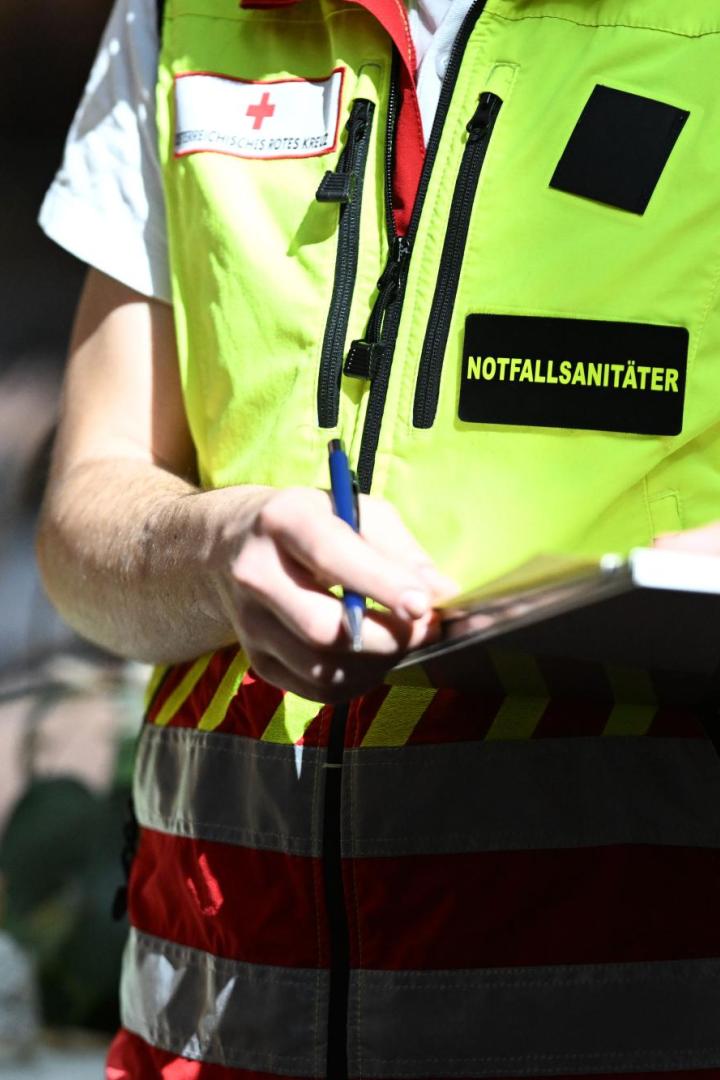 Ein Notfallsanitäter mit gelber Weste schreibt mit einem Stift auf ein Klemmbrett.