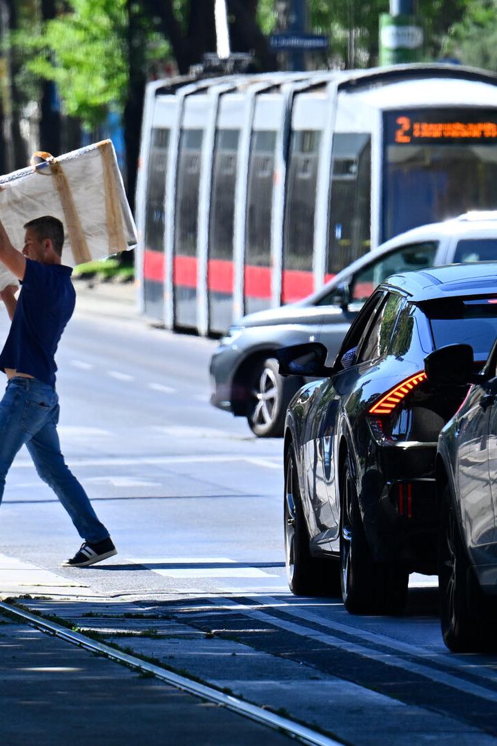 Ein Mann geht über die Straße, Autos warten, im Hintergrund fährt eine Straßenbahn.