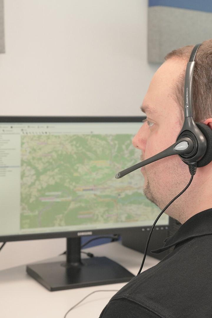 Ein Mann mit Headset sitzt vor mehreren Monitoren mit Karten- und Tabellendarstellungen.