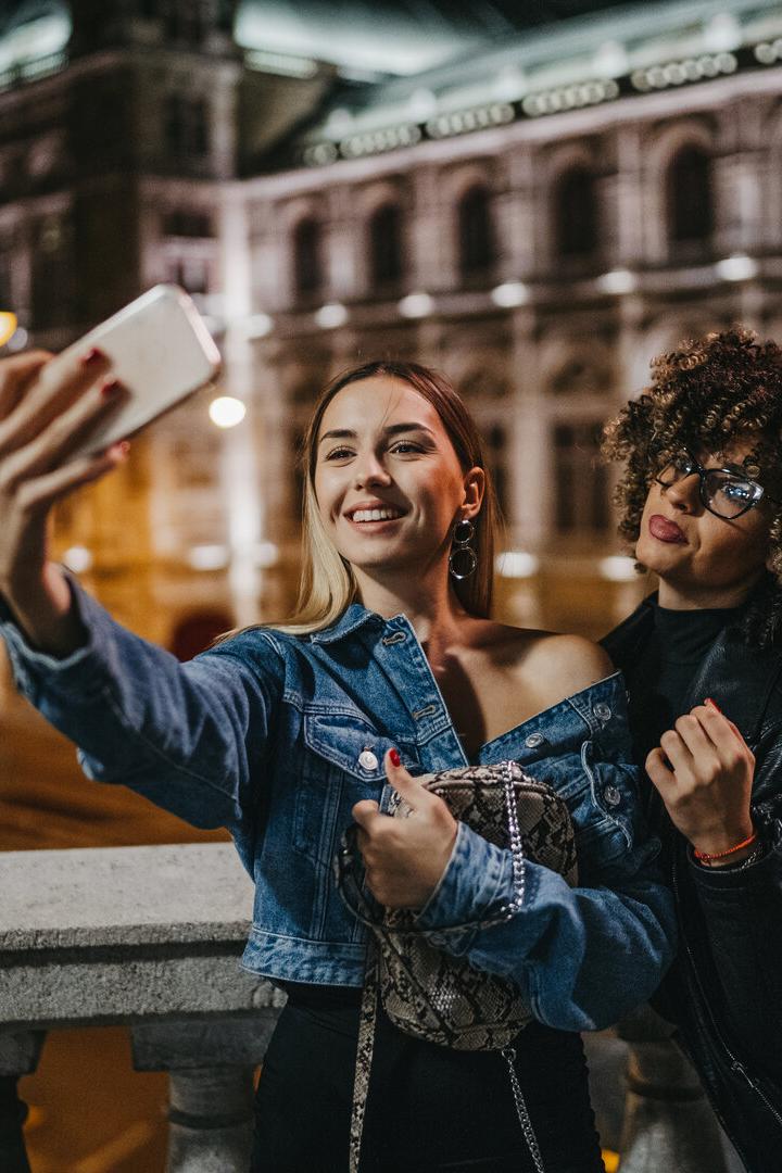 Zwei junge Frauen machen ein Selfie vor einem beleuchteten Gebäude in der Nacht.