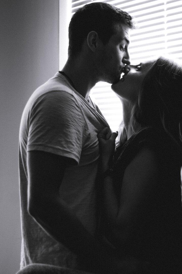 Ein Paar küsst sich leidenschaftlich vor einem Fenster mit Jalousien.