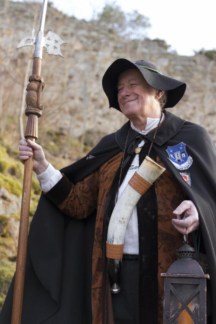 Ein Nachtwächter in traditioneller Kleidung mit Hellebarde, Horn und Laterne im Freien.
