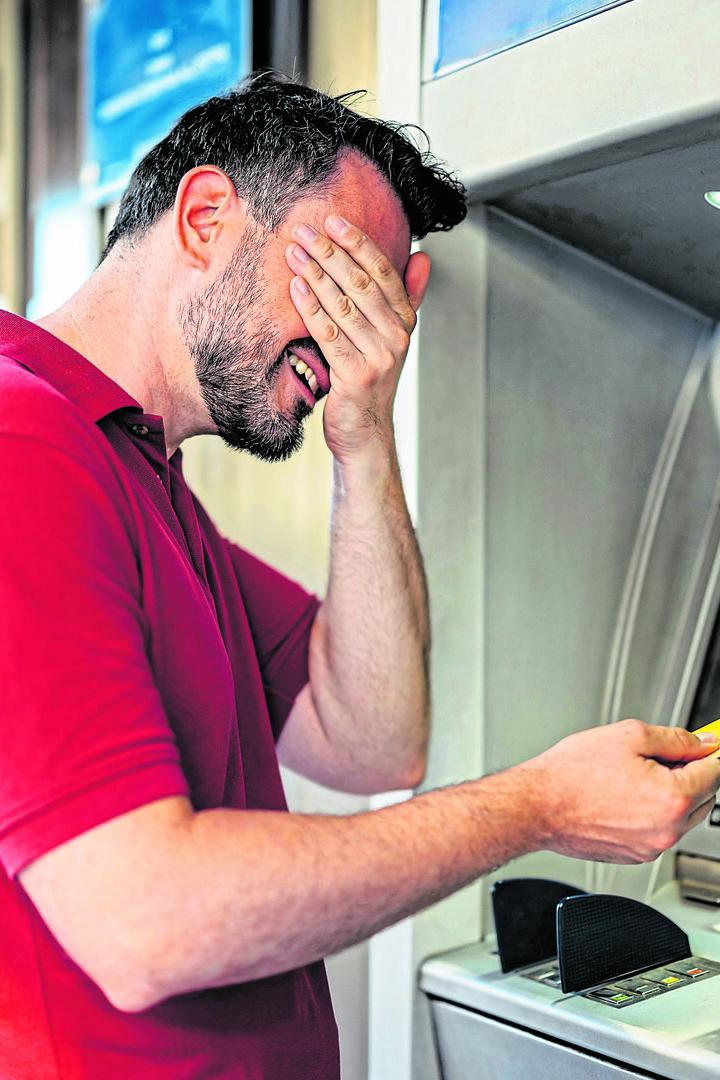 Mid-Adult Man Covering His Eyes Before Withdrawing Money Using A Credit Card At The ATM Machine