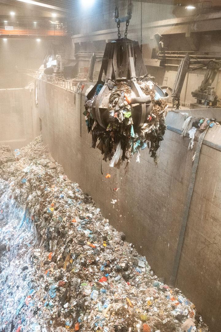 Eine Greifzange hievt Müll über einen riesigen Abfallbunker in einer Industrieanlage.