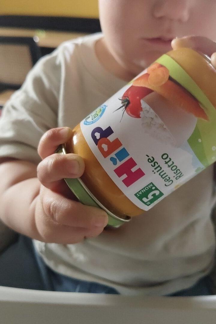 Ein Kleinkind hält ein Glas mit Hipp Gemüse Risotto Babynahrung in der Hand.