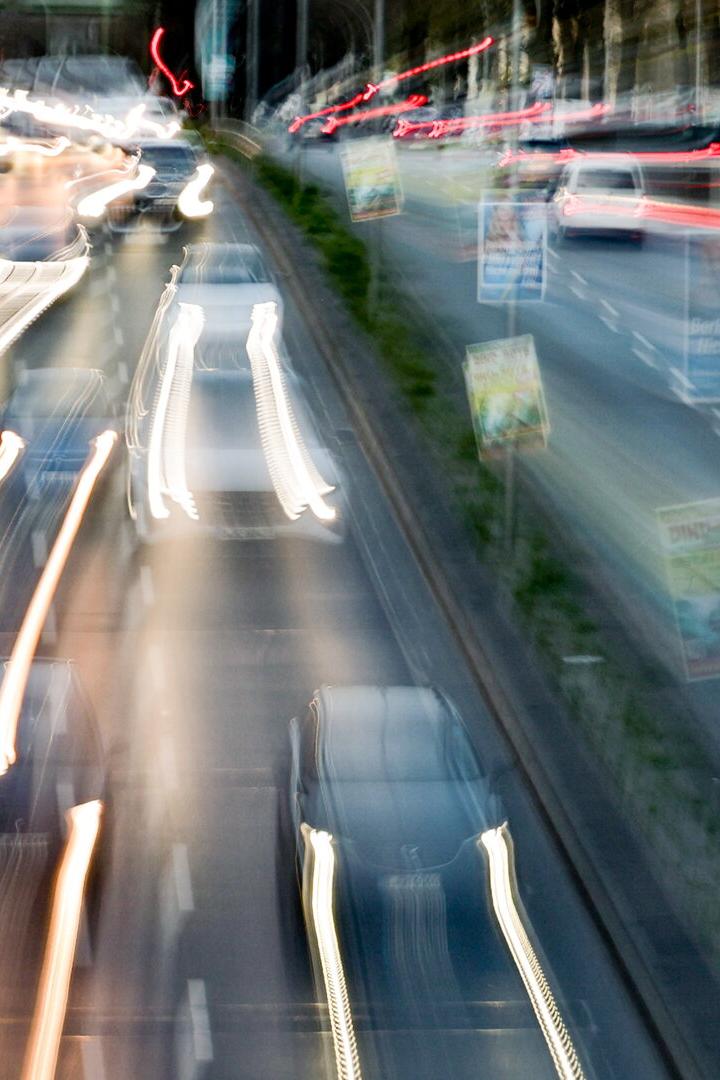 Mehrspurige Stadtautobahn mit vorbeifahrenden Autos und verschwommenen Lichtspuren bei Nacht.