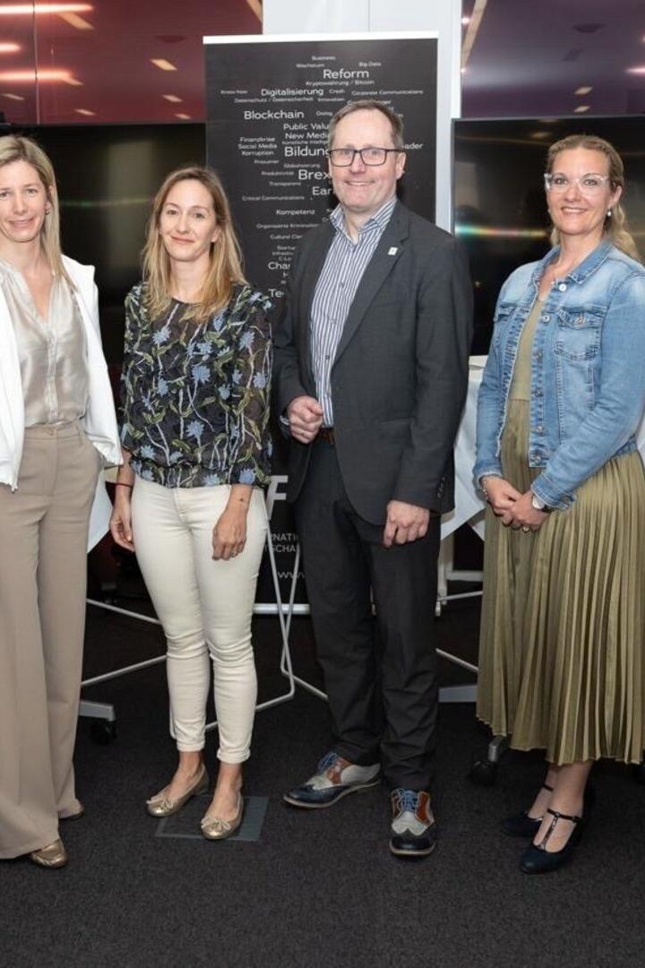 Sechs Personen stehen nebeneinander in Businesskleidung und lächeln in einer modernen Konferenzumgebung.