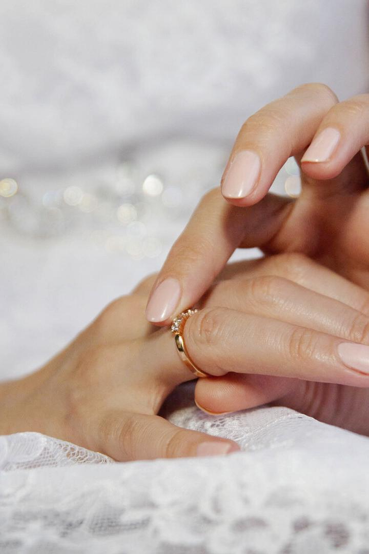 Eine Frau in weißer Spitze steckt sich einen goldenen Ring mit Stein an den Finger.