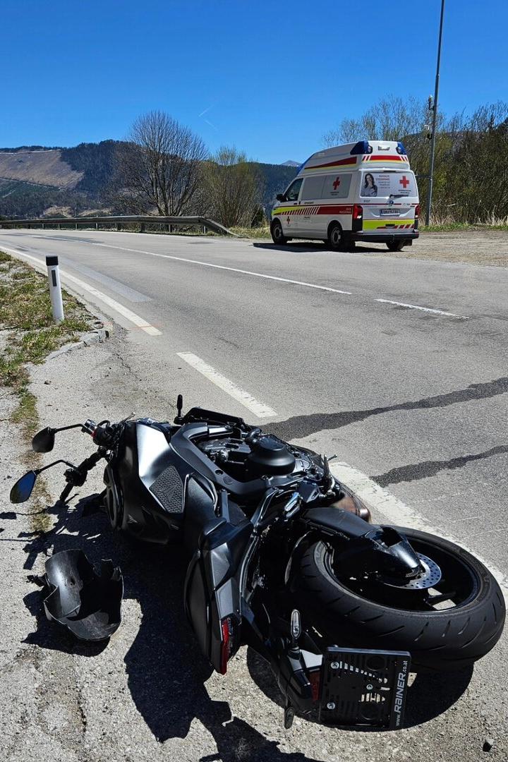 Ein Motorrad liegt umgestürzt am Straßenrand, daneben ein beschädigter Helm und ein Rettungswagen steht weiter vorne.