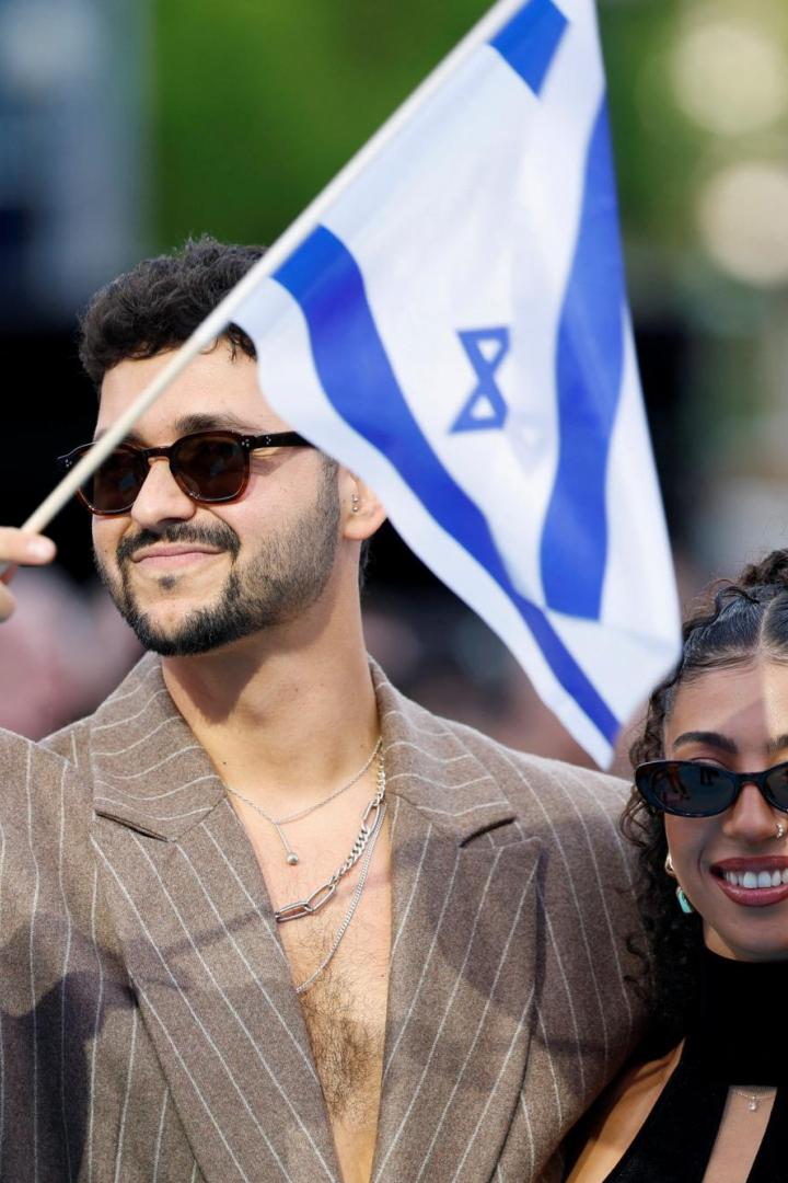 Ein Mann mit Sonnenbrille hält eine israelische Flagge, neben ihm stehen zwei lächelnde Frauen im Freien.