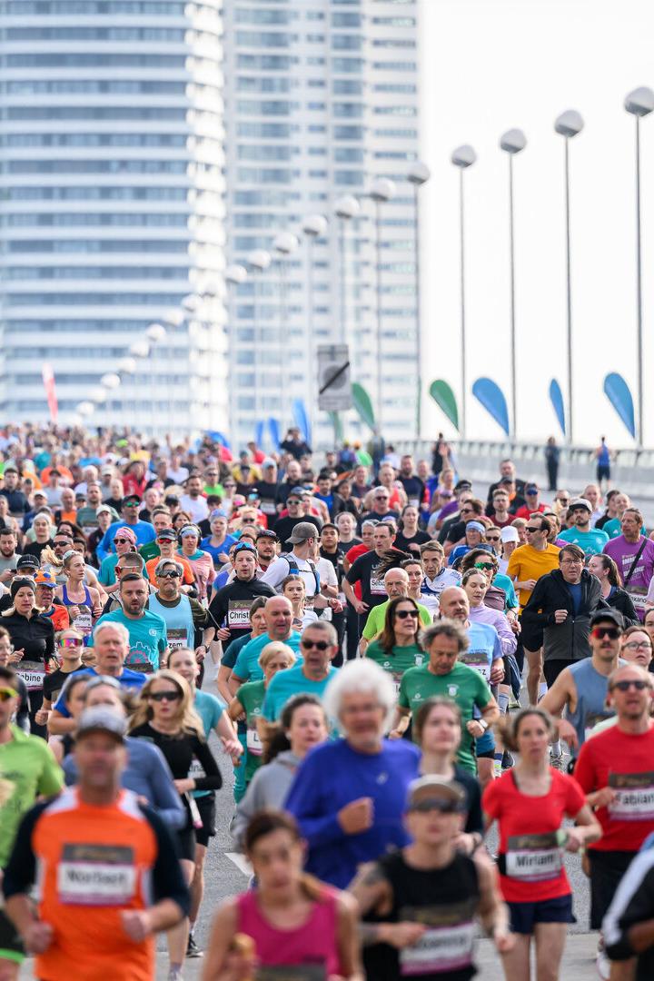 Viele Menschen laufen bei einem großen Stadtmarathon auf einer breiten Straße mit Hochhäusern im Hintergrund.