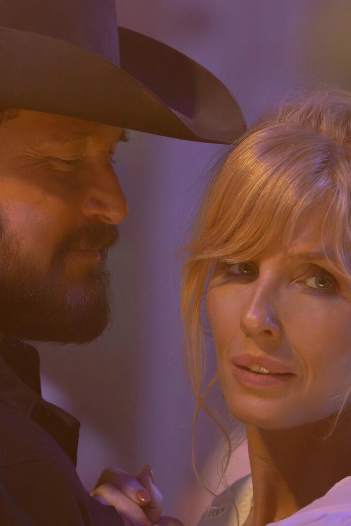 Ein Mann mit Bart und Cowboyhut tanzt eng mit einer blondhaarigen Frau, die nachdenklich in die Ferne blickt.