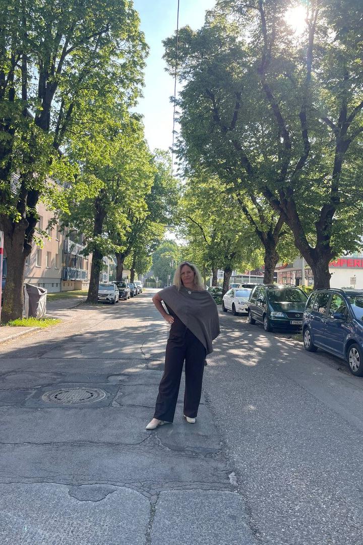 Eine Frau steht auf einer von Bäumen gesäumten Straße, umgeben von geparkten Autos und Sonnenschein.