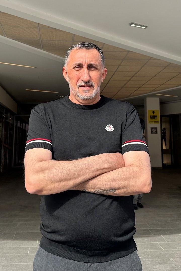 Ein Mann mit verschränkten Armen steht vor einem Einkaufszentrum mit H&M-Eingang im Hintergrund.
