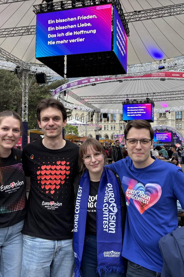 Vier Freunde posieren vor einer Bühne des Eurovision Song Contest in Wien.