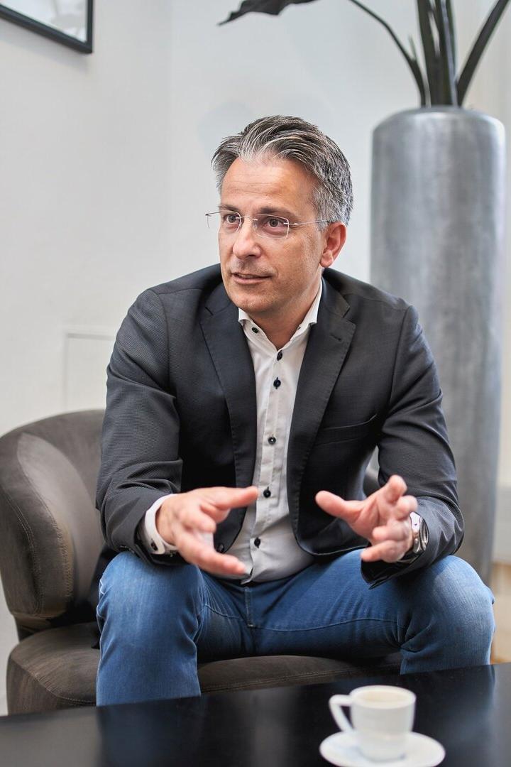 Ein Mann mit Brille, Sakko und Jeans sitzt gestikulierend in einem Sessel.