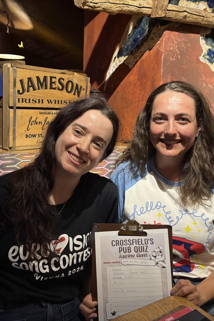Zwei Frauen lächeln mit einem "Crossfield's Pub Quiz"-Bogen und einem "Eurovision Song Contest"-T-Shirt.