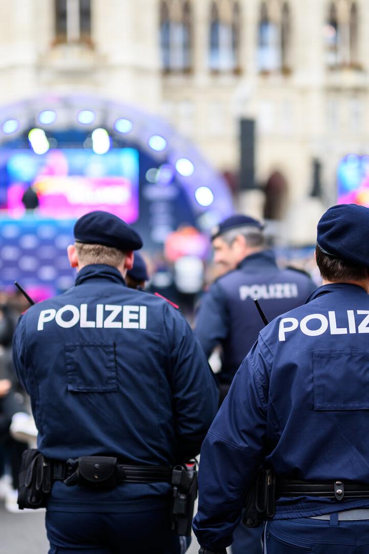 Mehrere Polizisten in Uniform überwachen eine Veranstaltung im Freien mit vielen Menschen und einer beleuchteten Bühne.