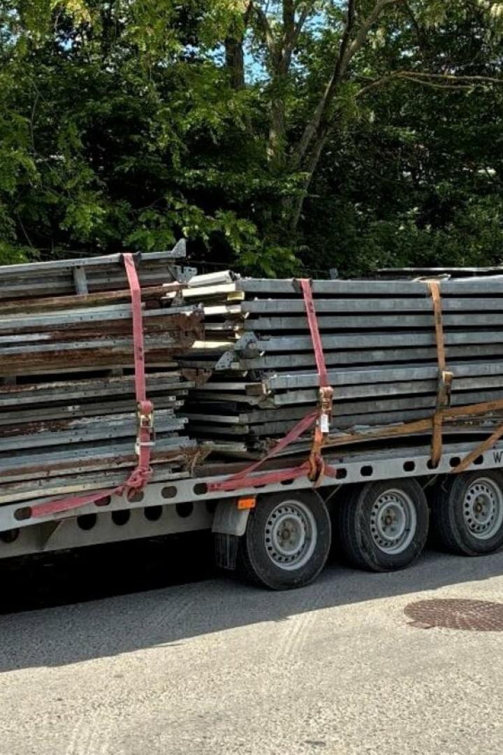 Ein weißer Transporter zieht einen Anhänger mit gestapelten Metallteilen, die mit Gurten gesichert sind.