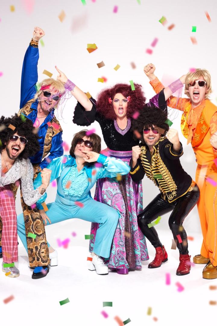 Sechs Personen in bunten 70er-Jahre-Outfits feiern ausgelassen mit Konfetti.