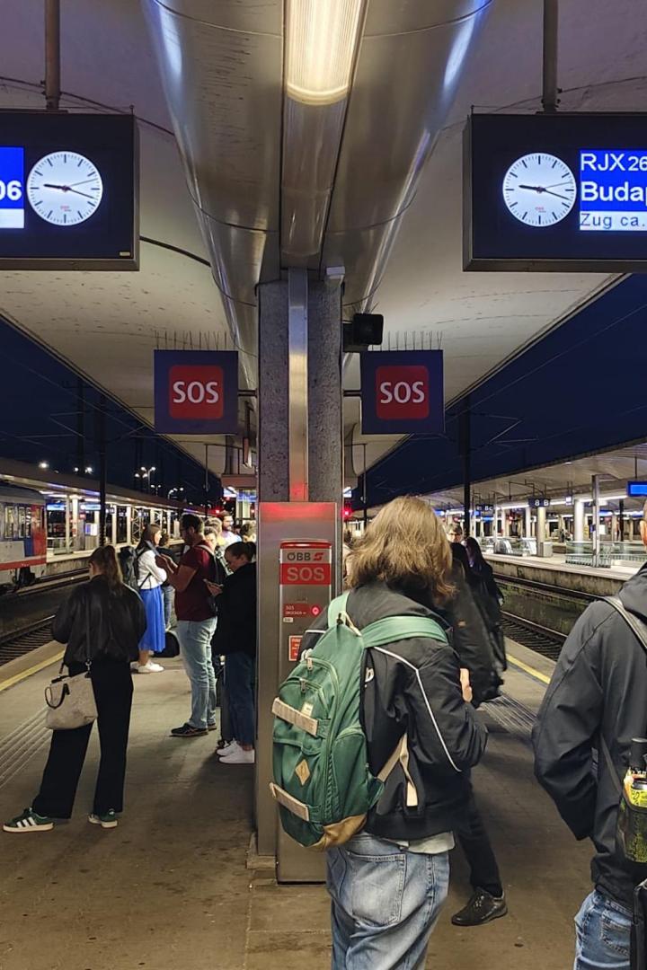 Bahnsteig in Linz mit Anzeigen und wartenden Fahrgästen.