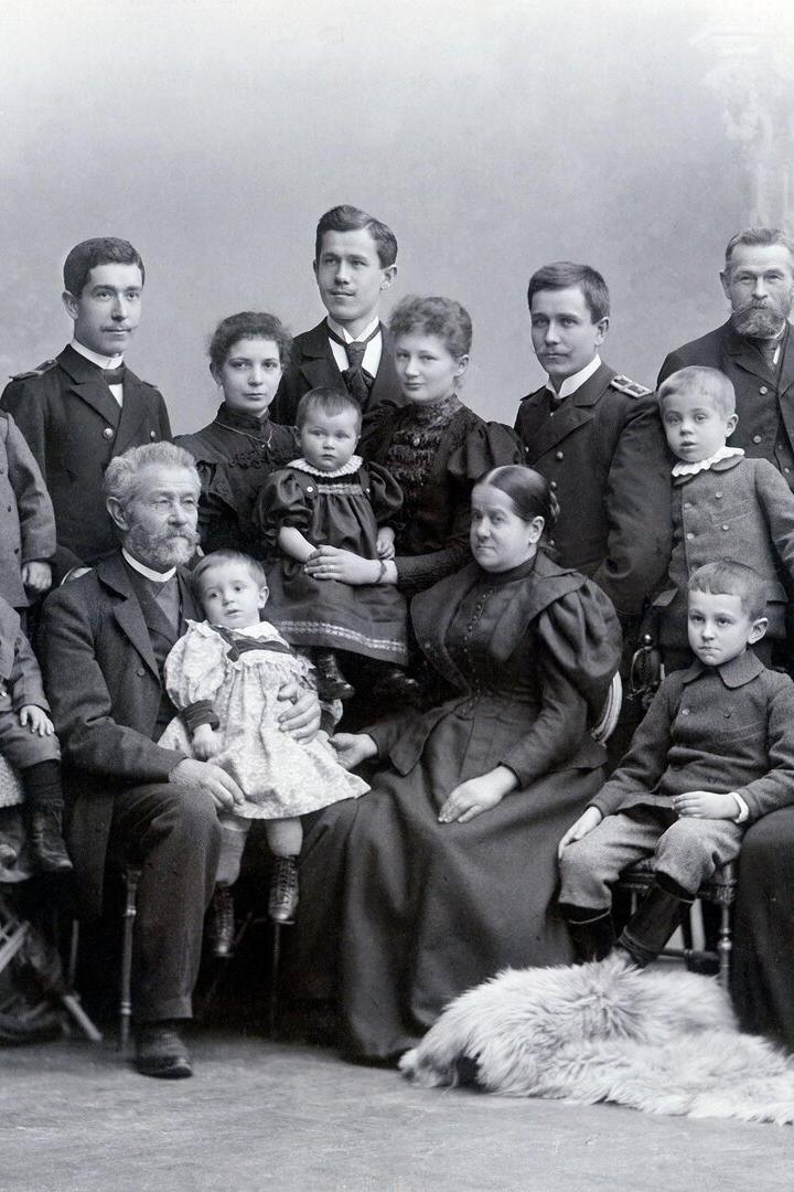 Eine große Familie posiert in altmodischer Kleidung für ein Schwarzweiß-Gruppenporträt.