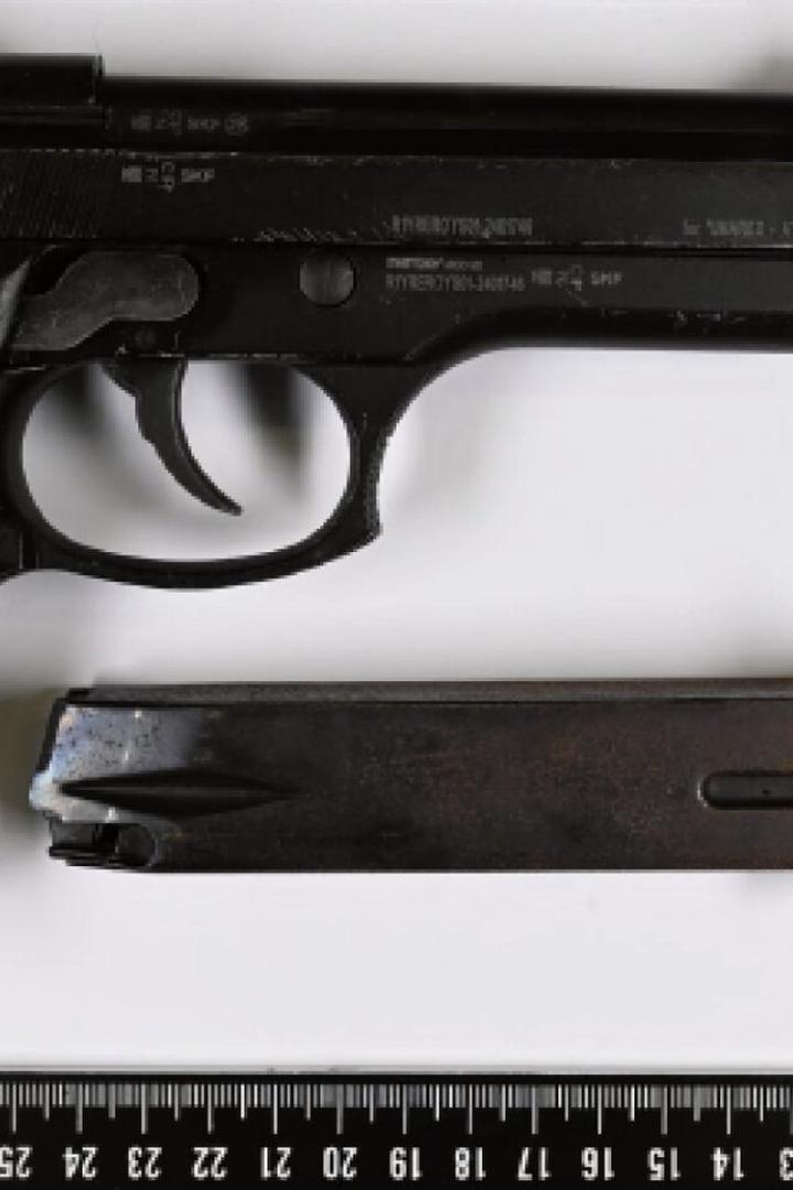Schwarze Pistole mit separatem Magazin liegt neben einem Lineal auf weißem Untergrund.