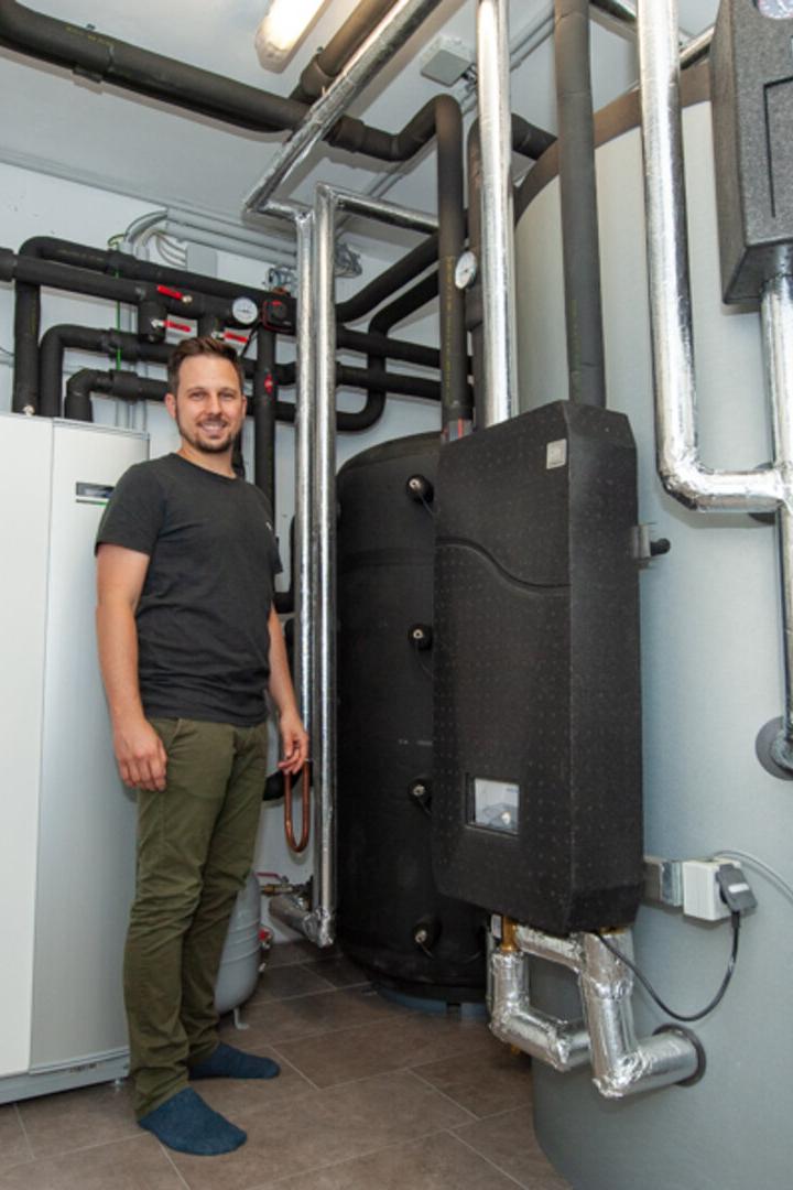 Ein Mann steht in einem Technikraum neben einer modernen Heizungsanlage mit vielen Rohren und Speichern.