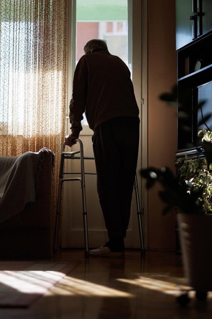 Elderly man with walker looking out window, contemplating life in quiet solitude