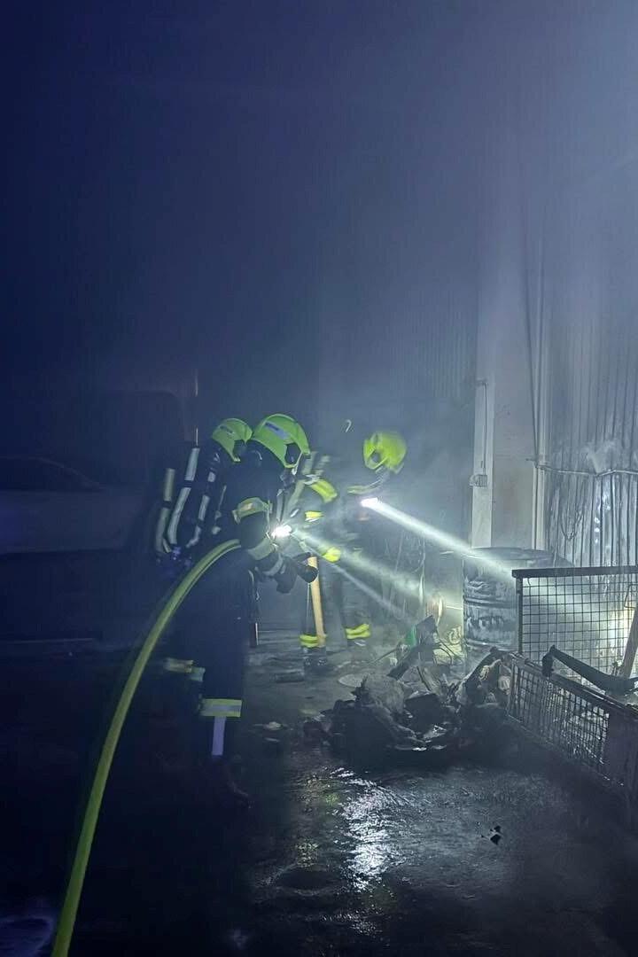 Zwei Feuerwehrleute mit Atemschutz löschen einen Brand in einer verrauchten Halle neben einem Getränkeautomaten.
