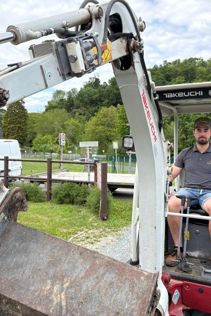 Ein Mann sitzt in einem kleinen Takeuchi-Bagger vor einer grünen Landschaft.