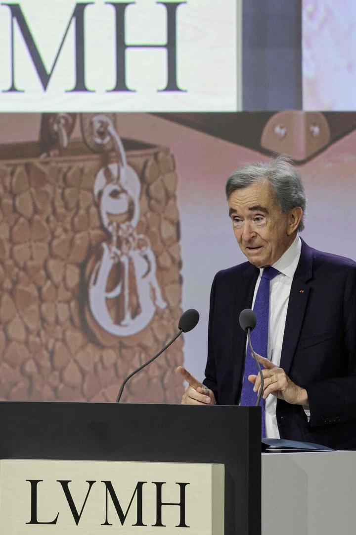 Bernard Arnault spricht vor einem LVMH-Logo, im Hintergrund eine Handtasche.
