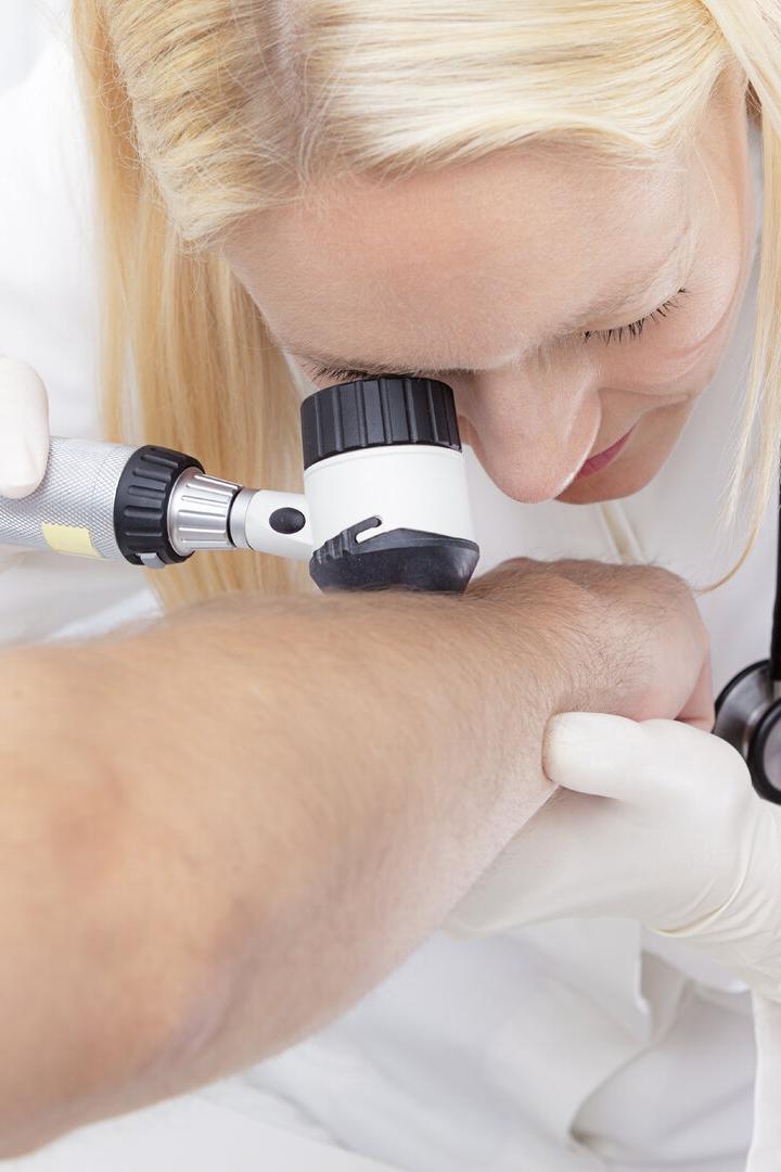 Eine Ärztin untersucht mit einem Dermatoskop die Haut am Arm eines Patienten.