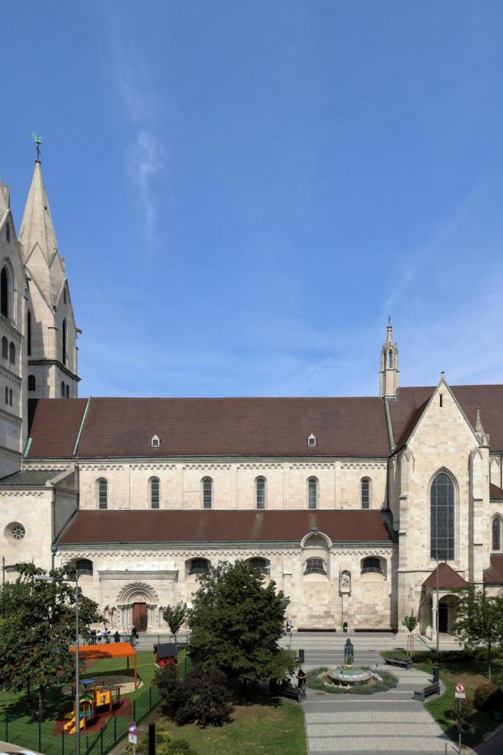 Große Kirche mit zwei hohen Türmen, rotem Dach und Spielplatz im Vordergrund an einem sonnigen Tag.