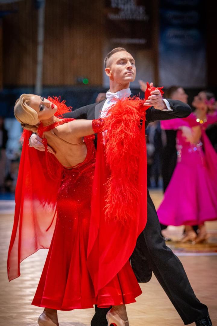 Ein elegantes Tanzpaar tanzt in festlicher Kleidung, die Frau trägt ein rotes Kleid mit Federn.