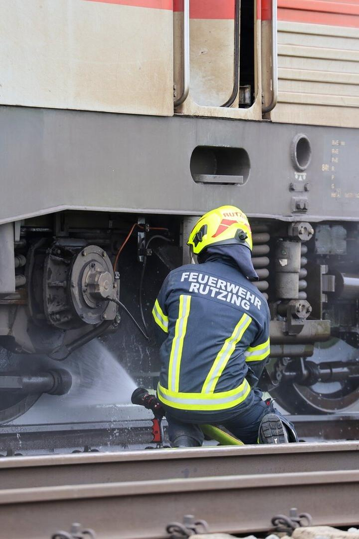 Ein Feuerwehrmann löscht mit einem Schlauch einen Brand am Fahrwerk eines Zuges auf den Gleisen.