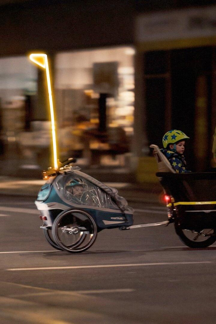 Ein Radfahrer fährt bei Dunkelheit mit einem Kind im Lastenrad und einem beleuchteten Fahrradanhänger über eine Straße.