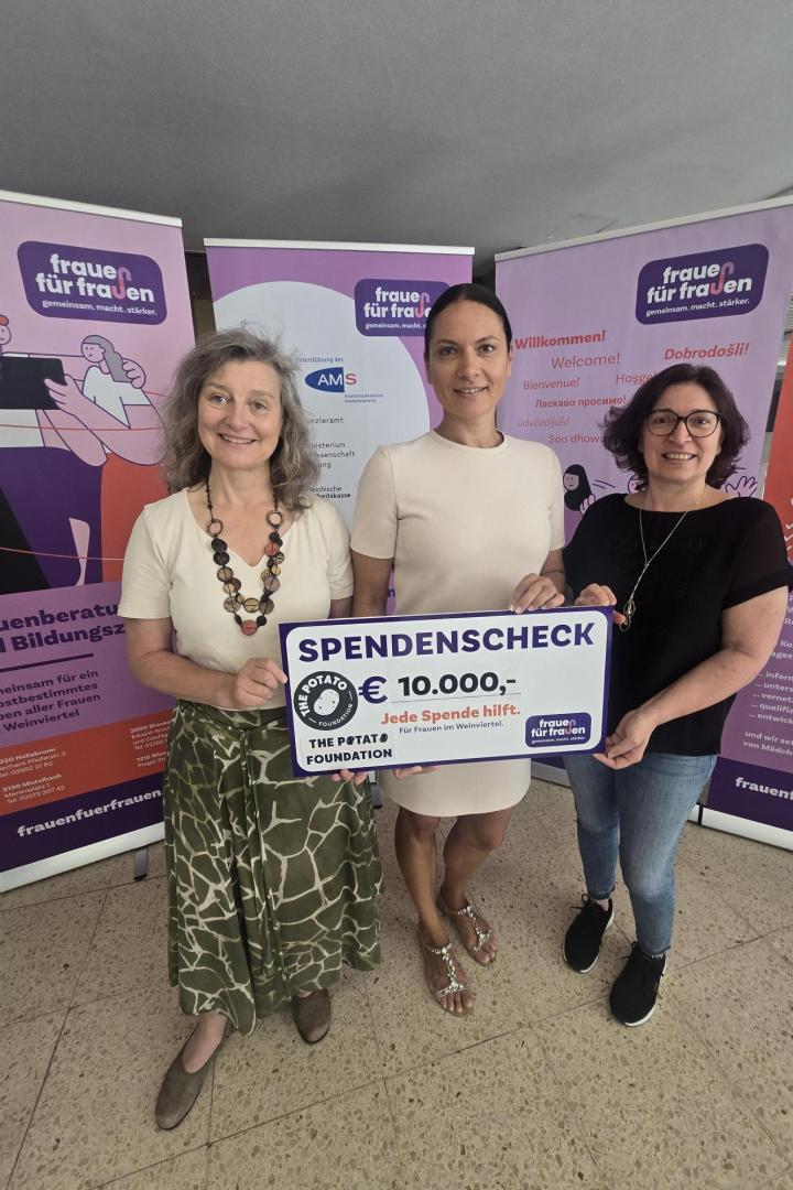 Drei Frauen halten einen Spendenscheck über 10.000 Euro vor Infotafeln von Frauen für Frauen.