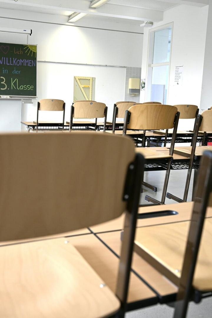 Leerer Klassenraum mit hochgestellten Stühlen und einer Tafel, auf der eine Willkommensbotschaft für die 3. Klasse steht.