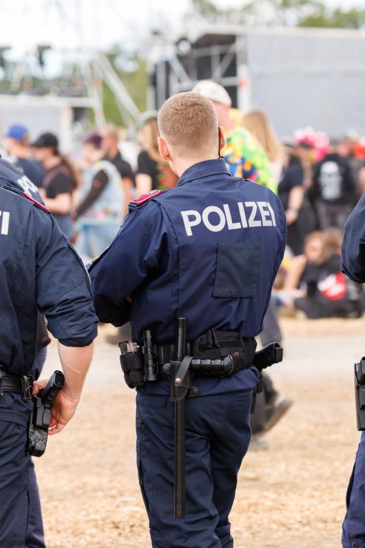 Mehrere Polizisten stehen mit dem Rücken zur Kamera vor einer Menschenmenge bei einer Veranstaltung.