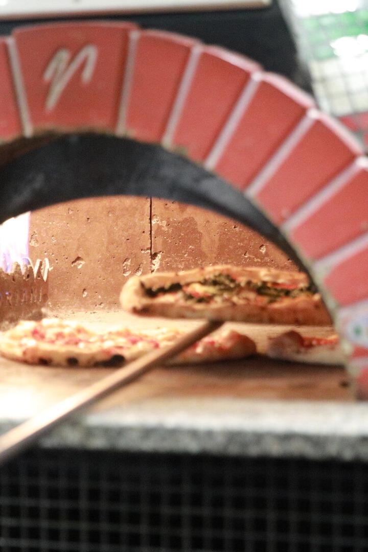 Zwei Pizzen werden mit einer Schaufel in einem traditionellen Steinofen gebacken.